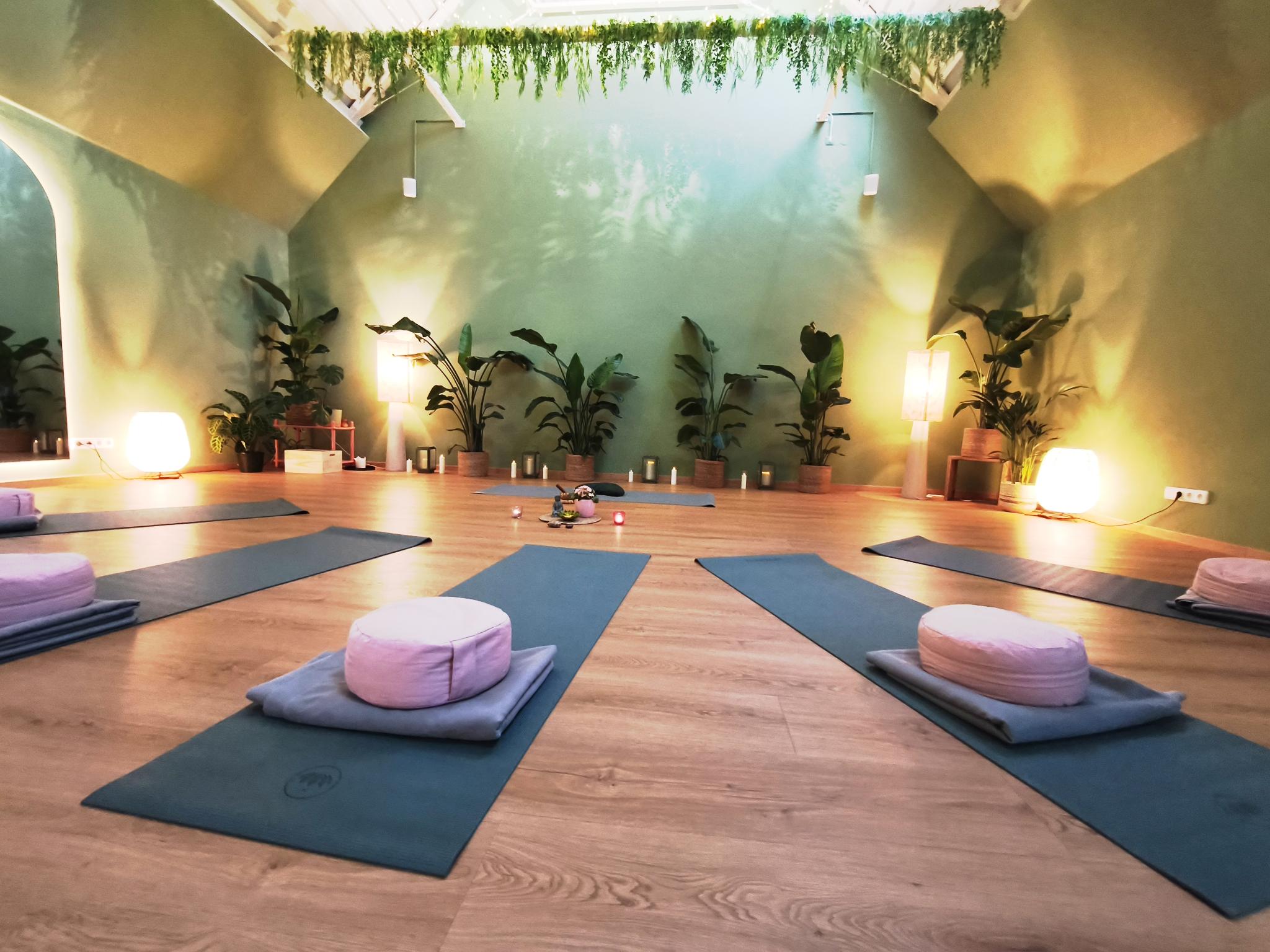 Yogastudio mit ausgelegten Yogamatten, Meditationskissen und Zimmerpflanzen in warmem, sanftem Licht